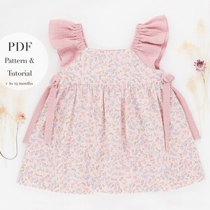 K&ouml;nnte beinhalten: Ein rosa-wei&szlig;es Babykleid mit floralem Muster, gekr&auml;uselten rosa &Auml;rmeln und rosa B&auml;ndern. Das Kleid ist f&uuml;r Babys von 1 bis 24 Monaten. Der Text "PDF Pattern & Tutorial" befindet sich auf einem wei&szlig;en Kreis.