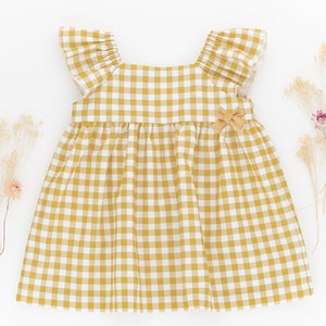 K&ouml;nnte beinhalten: Ein gelbes und wei&szlig;es Gingham-Kleid mit R&uuml;schen am Ausschnitt und kurzen &Auml;rmeln. Das Kleid hat eine Schleife an der Taille.
