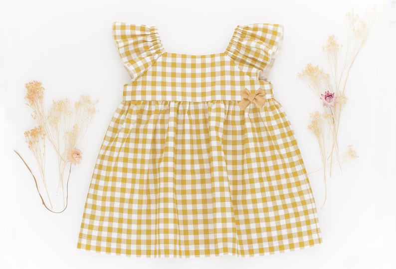 K&ouml;nnte beinhalten: Ein gelbes und wei&szlig;es Gingham-Kleid mit R&uuml;schen am Ausschnitt und kurzen &Auml;rmeln. Das Kleid hat eine Schleife an der Taille.
