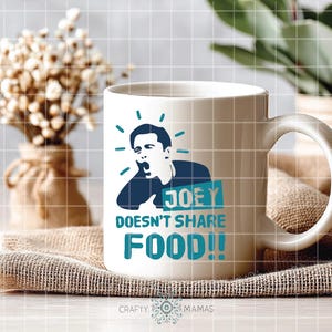 May include: White ceramic mug with a humorous design. The mug features a blue graphic of a person with the text "JOEY DOESN'T SHARE FOOD!!" in teal. The mug has a large handle and is sitting on a burlap cloth.