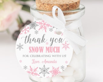 May include: Pink and silver snowflake thank you tags with the text "Thank you Snow Much" and "For celebrating with us! Love, Amanda". The tags are 2x2 inches and are attached to a small glass jar filled with white marshmallows.