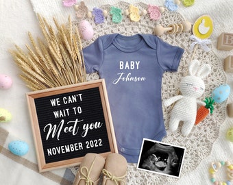 Könnte beinhalten: Eine Schwangerschaftsanzeige mit einem Buchstabenbrett, auf dem "We can't wait to meet you November 2022" steht. Es gibt einen Baby-Strampler mit der Aufschrift "Baby Johnson", ein gehäkeltes Häschen, Holzklötze, die "BABY" buchstabieren, und ein Ultraschallbild.