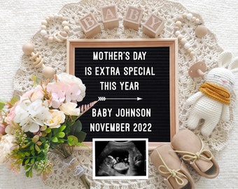 May include: A black letter board with the text "Mother's Day is extra special this year" and "Baby Johnson November 2022". A white crocheted bunny with a yellow scarf, a bouquet of pink and white flowers, and a pair of brown baby shoes are arranged around the letter board. A black and white ultrasound image is in the bottom right corner.