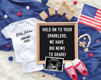 May include: A white baby onesie with the text "Baby Johnson January -2023-" is next to a letter board that says "HOLD ON TO YOUR SPARKERS, WE HAVE BIG NEWS TO SHARE!" An ultrasound image, baby shoes, and an American flag are also present.