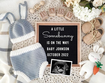 May include: A letter board with the text "A little Somebunny is on the way! Baby Johnson October 2022".  The board is surrounded by baby items, including a crocheted bunny hat, a pair of baby booties, a crocheted bunny toy, and a sonogram image.