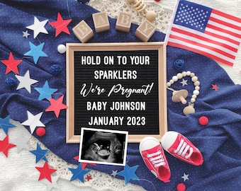 Könnte beinhalten: Eine Ankündigung mit dem Text "Hold on to your sparklers, We're Pregnant! Baby Johnson, January 2023." Die Ankündigung enthält ein Sonogramm, rote und weiße Babyschuhe und eine amerikanische Flagge. Dekorative Sterne und Holzblöcke buchstabieren "BABY".