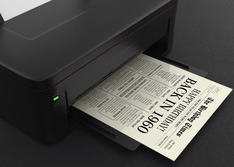 May include: A black printer with a white sheet of paper emerging from it. The paper has a newspaper design with the text "The Birthday Times" and "Happy Birthday! Back in 1960".