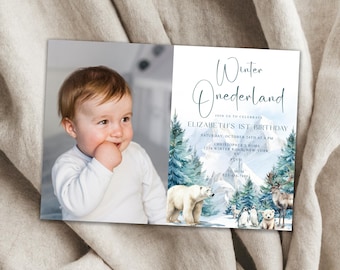May include: A blue and white winter wonderland themed first birthday party invitation with a photo of a baby boy. The invitation features a polar bear, penguins, and a reindeer in a snowy mountain scene. The text on the invitation reads "Winter Onederland" and includes the baby's name, birthday date, and time, and the location of the party.
