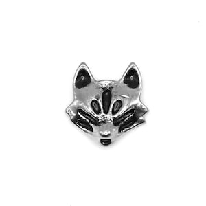 Puede incluir: Un amuleto de plata en forma de zorro con ojos negros y un diseño detallado. El amuleto es una pequeña pieza de joyería tridimensional.