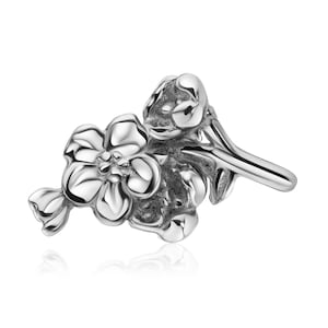 Pode incluir: Um berloque de prata em forma de um cacho de flores delicadas com um caule. O berloque é detalhado e realista.