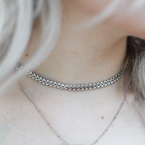 May include: A silver choker necklace with a delicate chain and a small pendant in the shape of a bird.