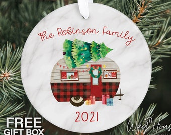 Op de afbeelding: Ronde kerstversiering met een marmerachtige achtergrond. De versiering toont een aquarel illustratie van een camper met een kerstboom erop. De tekst "The Robinson Family" en "2021" zijn in het rood geschreven. Een wit lint is bevestigd om op te hangen.