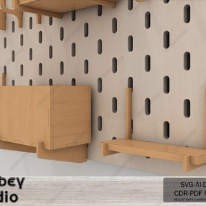 May include: A set of wooden shelves and storage boxes designed for a pegboard wall. The shelves are made of light brown wood and have a simple, modern design. The storage boxes are also made of light brown wood and have a rectangular shape. The pegboard wall is made of a light beige material and has a grid pattern of holes. The image includes the text "Atabey studio" and "SVG-AI-DXF CDR-PDF FILES READY EASY LASER CUT FILES".