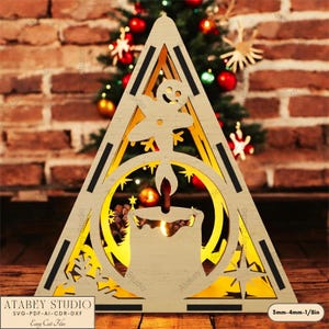 May include: A wooden Christmas tree-shaped decoration with a candle and gingerbread man design. The decoration has a light-colored wood frame with black accents and the text "ATABEY STUDIO" and "Easy Cut Files". The candle is in a circular frame.