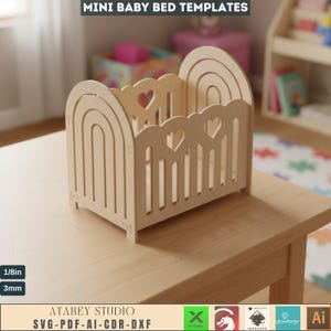 Puede incluir: Una cama de bebé de madera en miniatura con un acabado natural. La cama presenta un diseño recortado en forma de corazón y cabecero y piecero arqueados. Los textos "MINI BABY BED TEMPLATES" y "ATABEY STUDIO" son visibles.