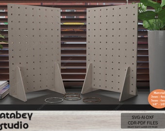 May include: Two beige pegboards with triangular bases, each with a grid of evenly spaced holes. The pegboards are standing on a table with a few silver and copper rings in front of them. The text "Atabey studio" is at the bottom left of the image. The text "Material 3mm-4mm 5mm-6mm 1/4"-1/8" SVG-AI-DXF CDR-PDF FILES READY EASY LASER CUT FILES" is at the bottom right of the image.