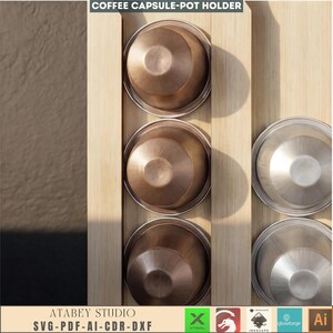 Puede incluir: Un portac&aacute;psulas de caf&eacute; de madera con tres c&aacute;psulas de caf&eacute; de color bronce y tres tapas de color plateado. El soporte es de madera clara. El texto "COFFEE CAPSULE-POT HOLDER" est&aacute; en la parte superior. El texto "ATABEY STUDIO SVG-PDF-AI-CDR-DXF" est&aacute; en la parte inferior.