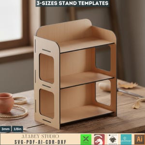 May include: A three-tiered wooden stand with a light brown finish and black edges. The stand has a rectangular shape with open sides and is labeled "3-SIZES STAND TEMPLATES". The text "ATABEY STUDIO SVG-PDF-AI-CDR-DXF" is also visible.