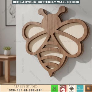 May include: A wooden wall decor piece in the shape of a bee. The bee is made of layered wood, with a light-colored interior and a darker, wood-grain exterior. The text "BEE-LADYBUG-BUTTERFLY WALL DECOR" is at the top. The bottom of the image has the text "ATABEY STUDIO" and "SVG-PDF-AI-CDR-DXF".