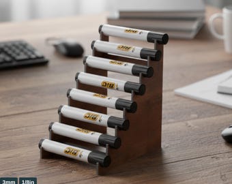 May include: A wooden pencil holder with a stepped design, holding eight white and black BIC markers. The text "PENCIL HOLDER TEMPLATE" is at the top. The holder is on a wooden surface. The bottom of the image includes the text "ATABEY STUDIO SVG-PDF-AI-CDR-DXF".
