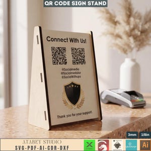 May include: A wooden QR code sign stand with the text "Connect With Us!" and social media handles. The stand features a black and gold emblem and the text "Thank you for your support." The stand is 1/8 inch thick.