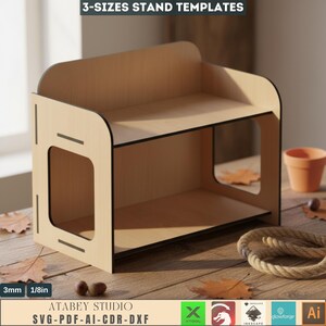 May include: A wooden stand with two shelves and a rectangular cutout on the side. The stand is made of light-colored wood with black trim. The text "3-SIZES STAND TEMPLATES" and "ATABEY STUDIO SVG-PDF-AI-CDR-DXF" are visible. The stand is 1/8in thick.