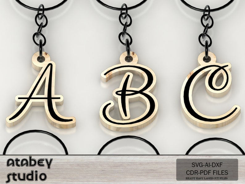 May include: Three wooden keychains with the letters A, B, and C in a cursive font. The letters are light brown with black outlines and are attached to black metal chains. The keychains are displayed against a white background. The text "Atabey studio" and "SVG-AI-DXF CDR-PDF FILES READY EASY LASER CUT FILES" are visible.