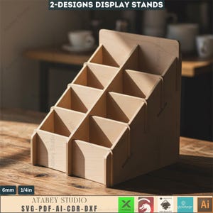 Può includere: Un espositore in legno marrone chiaro con più scomparti, ideale per organizzare piccoli oggetti. L'espositore presenta un design a gradini con diverse sezioni triangolari e rettangolari. Il testo "2-DESIGNS DISPLAY STANDS" è in alto. Lo spessore è di 6 mm.
