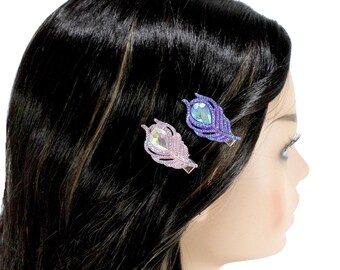 Puede incluir: Dos pinzas para el pelo con forma de pluma adornadas con joyas. Una pinza es morada con una gema azul claro, la otra es rosa con una gema rosa claro.