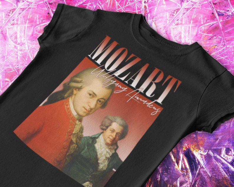 May include: Black t-shirt featuring a vintage-style graphic of Wolfgang Amadeus Mozart. The graphic depicts a portrait of Mozart and another man, with the text "Mozart" in large white letters and "Wolfgang Amadeus" in smaller white letters.