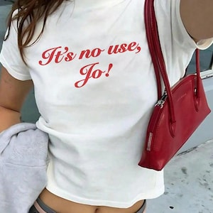 May include: White t-shirt with red text that says "It's no use, Jo!" The person is wearing a red handbag and a grey skirt with a pink belt.