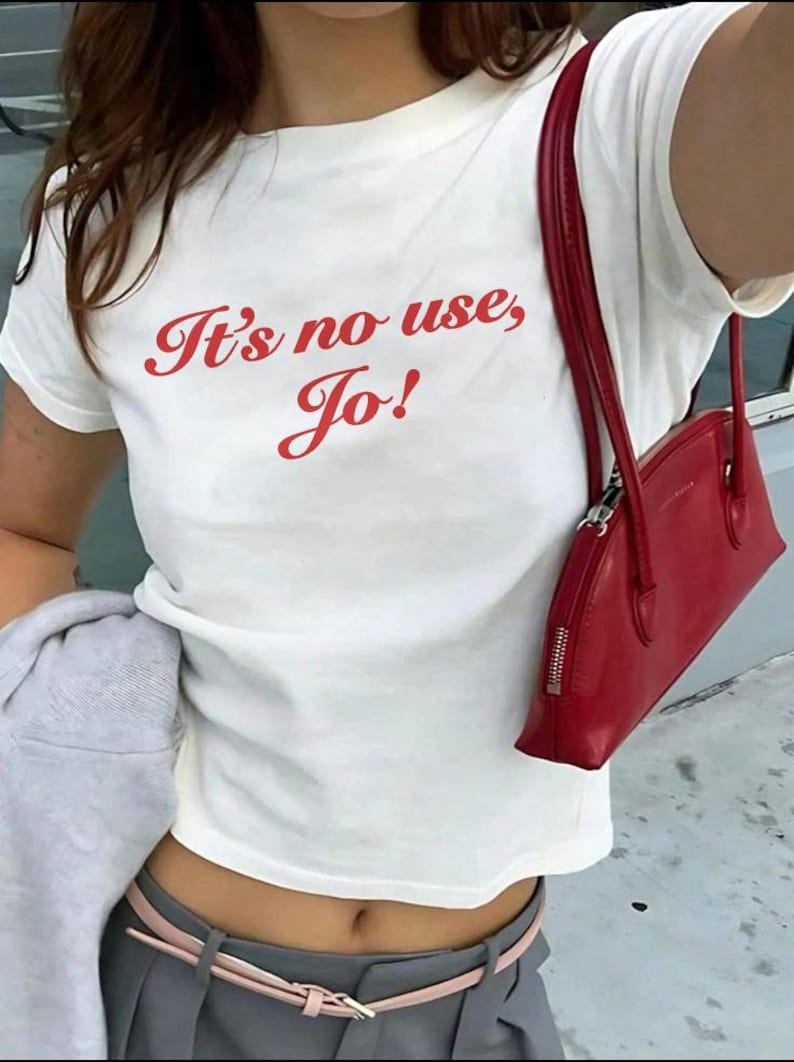 May include: White t-shirt with red text that says "It's no use, Jo!" The person is wearing a red handbag and a grey skirt with a pink belt.