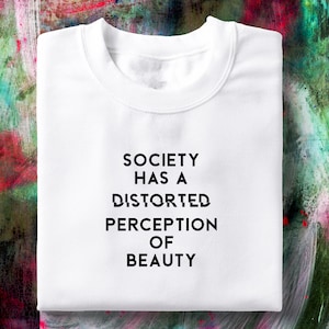 May include: White t-shirt with the text "SOCIETY HAS A DISTORTED PERCEPTION OF BEAUTY" printed in black.