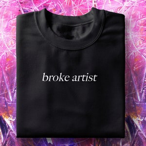 Puede incluir: Camiseta negra con el texto "broke artist" impreso en blanco en la parte delantera.