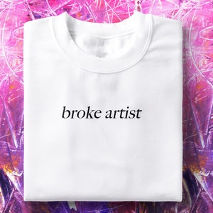 Puede incluir: Sudadera blanca de cuello redondo con el texto "broke artist" impreso en negro en la parte delantera.