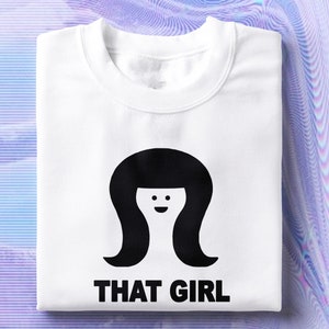 May include: White sweatshirt with a black silhouette of a woman with a bob haircut and a smiling face. The text "THAT GIRL" is printed below the silhouette.