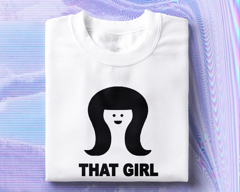 May include: White sweatshirt with a black silhouette of a woman with a bob haircut and a smiling face. The text "THAT GIRL" is printed below the silhouette.