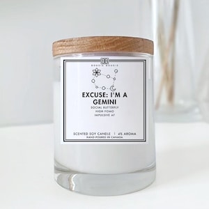 May include: A white candle with a wooden lid and a black label that reads "Excuse: I'm a Gemini" with a zodiac symbol and the text "Social Butterfly, High Fomo, Impulsive AF". The label also says "Scented Soy Candle | 4% Aroma | Hand-Poured in Canada".