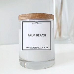 May include: A white soy candle with a wooden lid and a label that reads "BOUGIE BOUGIE" and "PALM BEACH". The label also says "SCENTED SOY CANDLE | 4% AROMA" and "HAND-POURED IN CANADA".