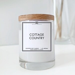 May include: A white soy candle with a wooden lid and a label that reads "BOUGIE BOUGIE", "COTTAGE COUNTRY", "SCENTED SOY CANDLE | 4% AROMA", and "HAND POURED IN CANADA".