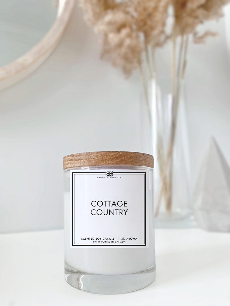 May include: A white soy candle with a wooden lid and a label that reads "BOUGIE BOUGIE", "COTTAGE COUNTRY", "SCENTED SOY CANDLE | 4% AROMA", and "HAND POURED IN CANADA".