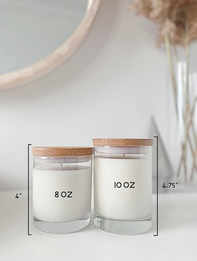 May include: Two glass candle jars with wooden lids. The smaller jar is 8 oz and the larger jar is 10 oz. The jars are on a white surface.