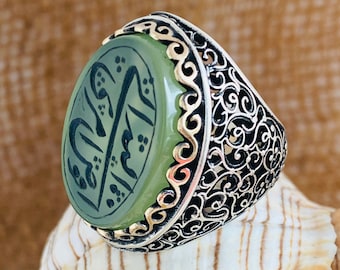 May include: A silver ring with an oval green stone featuring Arabic calligraphy. The ring has a filigree design.