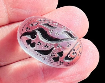 May include: A clear oval-shaped stone with intricate black and silver floral designs carved into the surface.