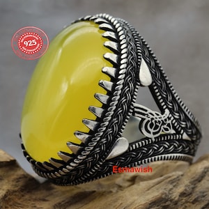 May include: A silver ring with a yellow oval gemstone set in a detailed, intricate design. The ring features a braided band with a triangular cutout and a heart-shaped design on each side. The ring is stamped "925 Sterling Silver".