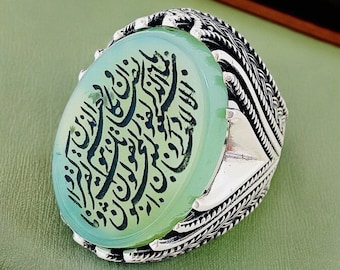 May include: A silver ring with a green stone featuring Arabic calligraphy. The ring has a detailed, intricate design.