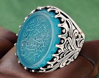 May include: A silver ring with a blue agate stone set in a detailed floral design. The stone has Arabic script engraved on it.