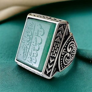 May include: A silver ring with an ornate design and a green stone set in the center. The stone has Arabic calligraphy etched into it.