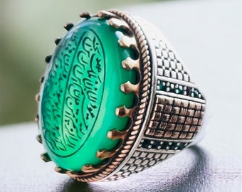 May include: A silver ring featuring a large oval green stone set in an ornate silver and gold band. The stone is engraved with Arabic script.