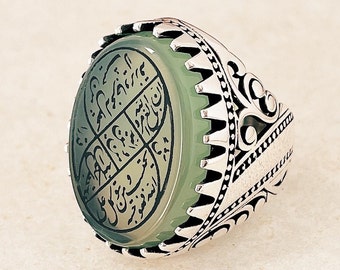 May include: A silver ring with a green stone featuring Arabic calligraphy. The ring has a detailed, ornate design.